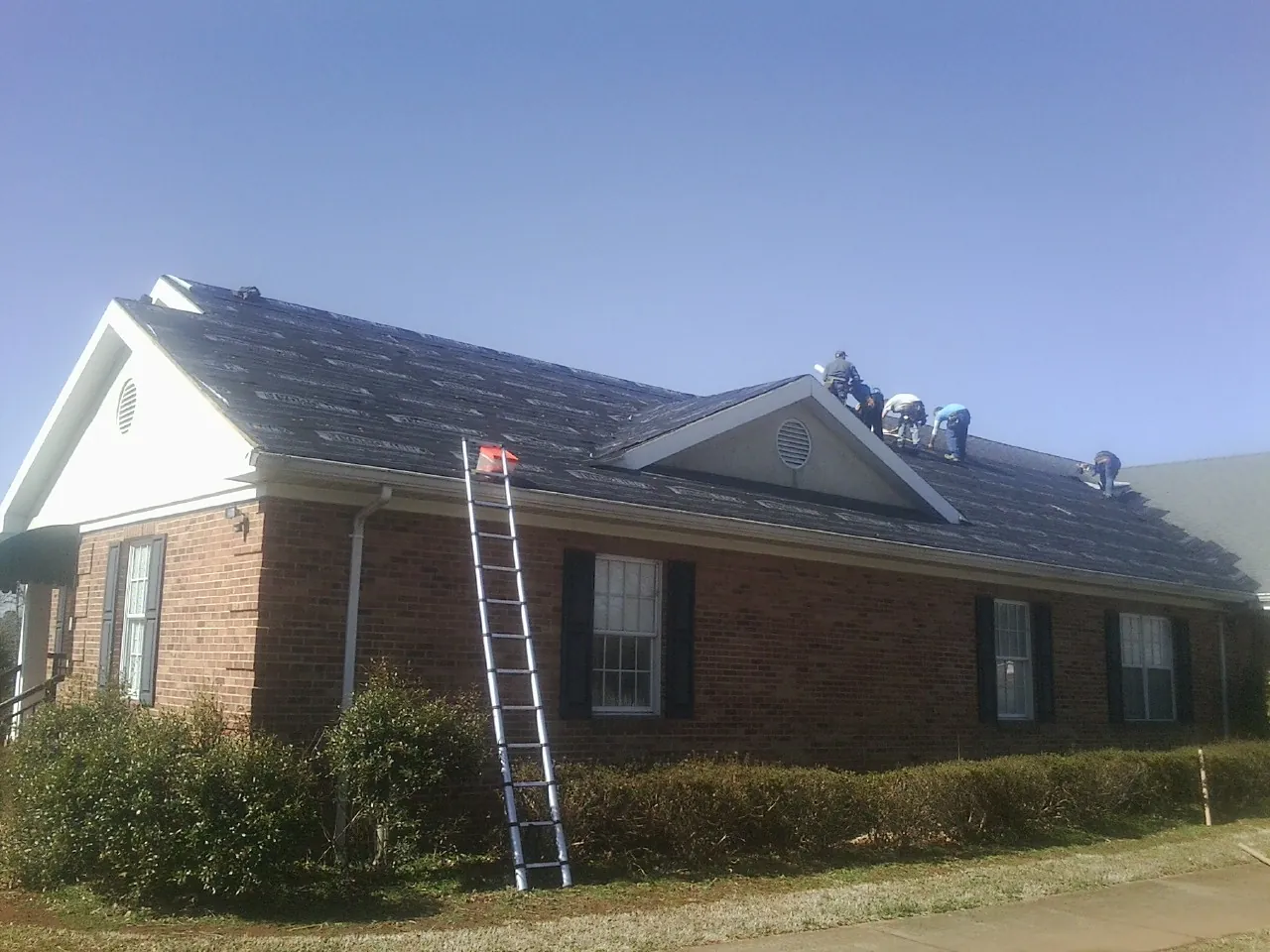 Crew tearing shingles off a brick ranch roof with a ladder set — Emergency Roof Repair work by our crew in Oakley