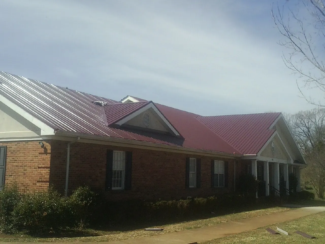 Red metal roof with gabled entries on a long brick building, from a Hail Damage Roof Repair job in Oakley